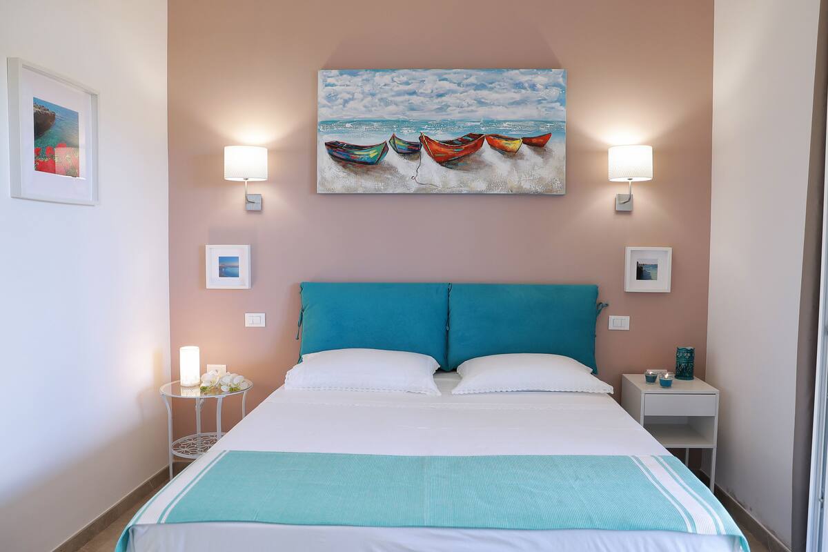 Ein Schlafzimmer mit einem Bett, zwei Nachttischen, einem Wandbild und einem Beistelltisch.