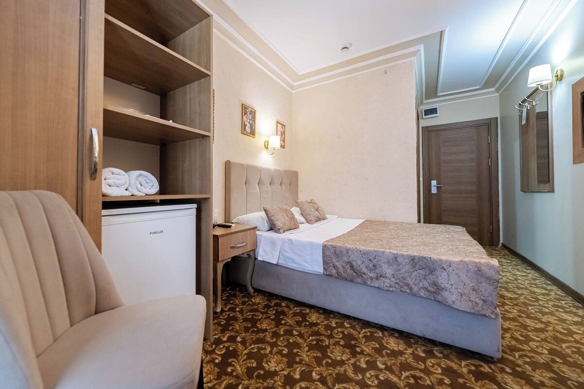A hotel room with a bed, a desk, a wardrobe, and a small refrigerator.