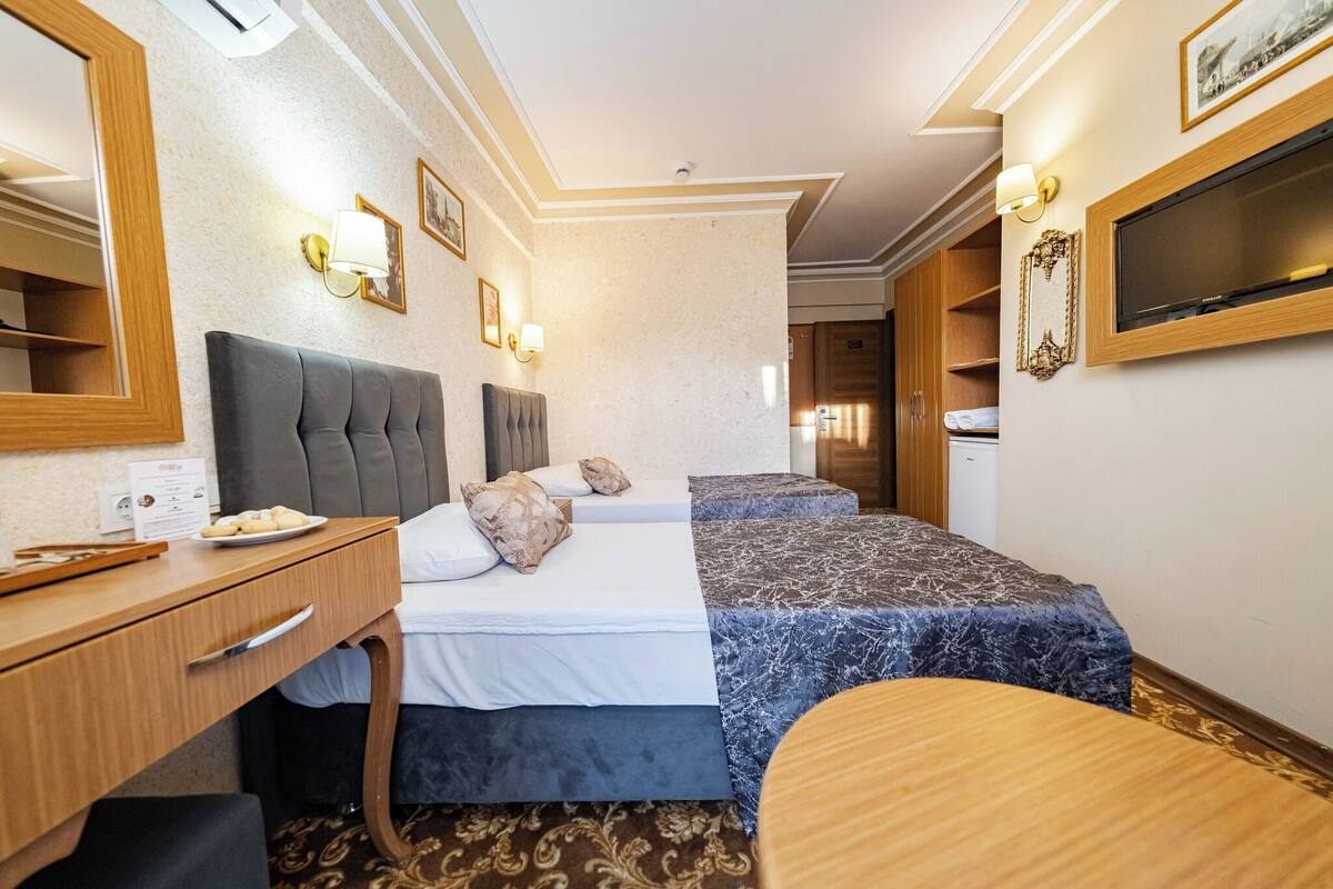 A hotel room with a bed, bedside table, lamp, and a television mounted on the wall.