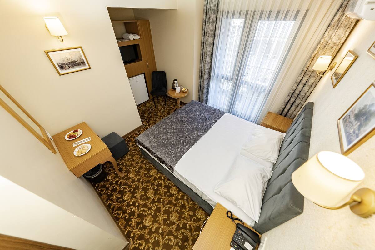 A hotel room with a bed, a small table with a plate of food, a chair, a desk with a telephone, and a wardrobe.