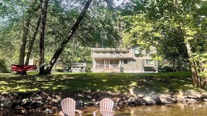 A house with a deck and a pond with two Adirondack chairs.