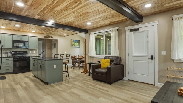 A modern kitchen with a central island, dining area with a table and chairs, and a living room with a sofa and a door.