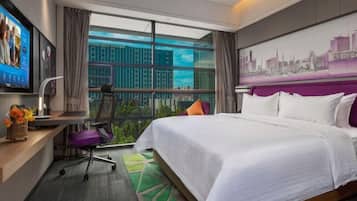 A hotel room with a large bed, a desk with a computer, a chair, and a TV.