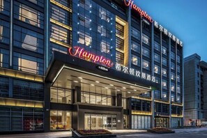 Un hotel moderno con un llamativo letrero de 'Hampton', grandes ventanales y una entrada bien iluminada.