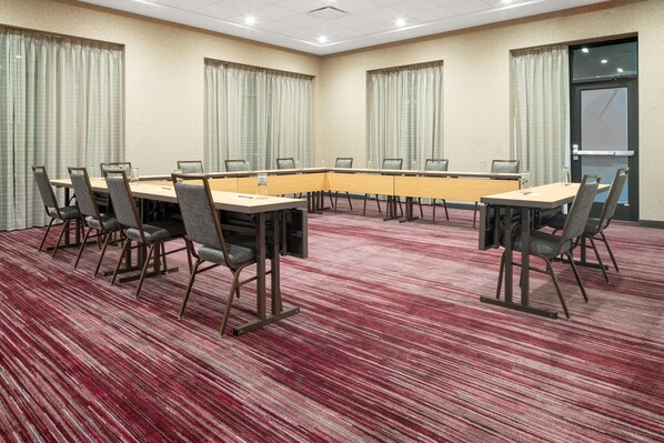 Una sala de conferencias con una larga mesa y sillas, piso alfombrado y cortinas en las ventanas.