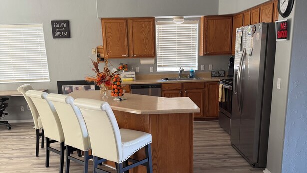 A modern kitchen with wooden cabinets, a stainless steel refrigerator, and a dining area with a table and chairs. - Sheppard 3bd1ba FtHuaSierraVista baby-massage (Sierra Vista)