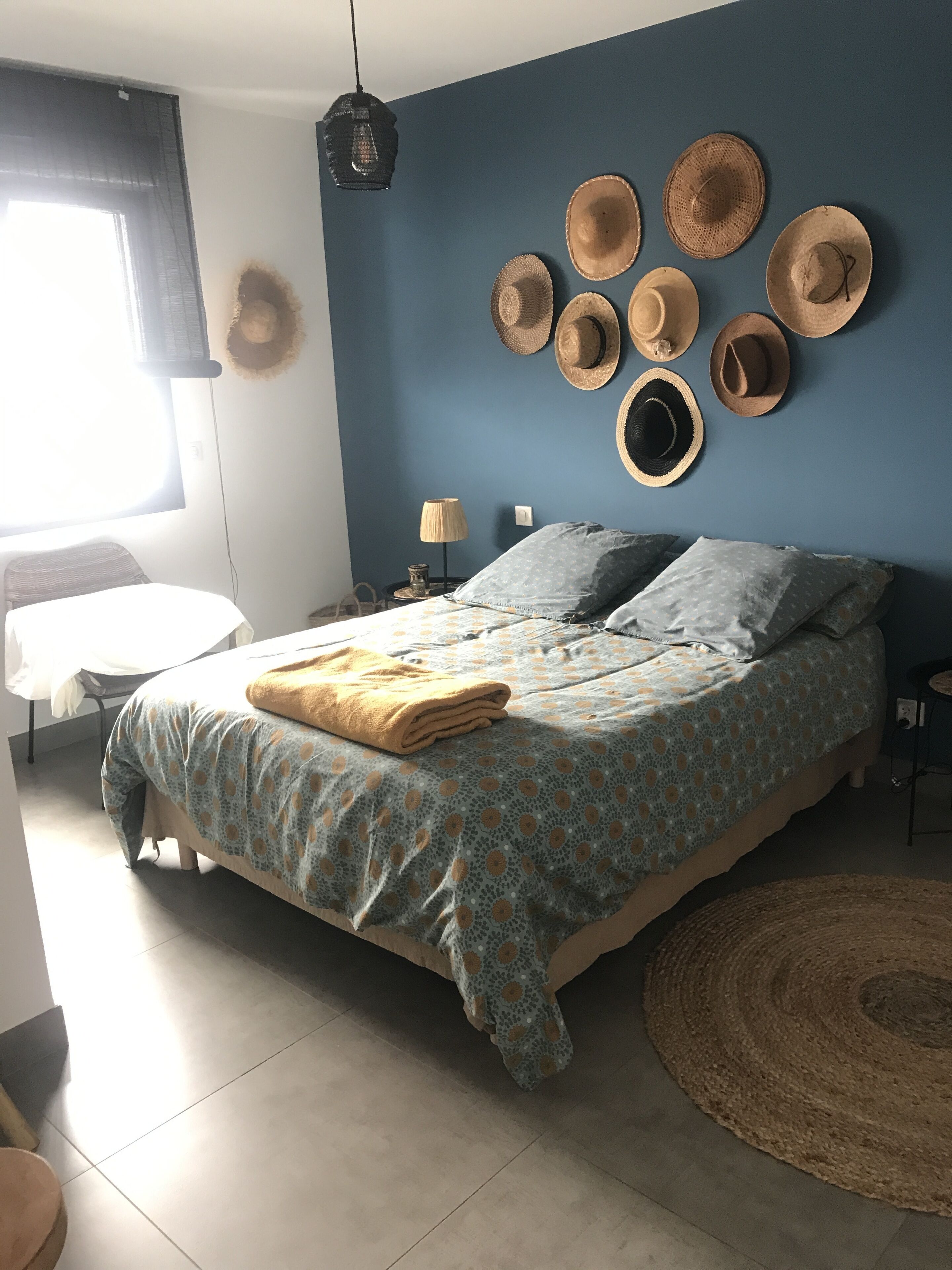 Un dormitorio con una cama, almohadas, una mesita de noche, una lámpara y una pared decorada con sombreros.