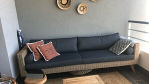 A dark-colored sofa with two pillows, a woven basket, a small wooden stool, and a woven mat on the floor. - Bastia : Apartment facing the sea, 2 beaches nearby  (San-Martino-di-Lota)