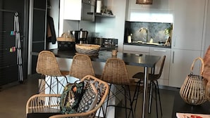 A modern kitchen with white cabinets, a central island, and wicker chairs. - Bastia : Apartment facing the sea, 2 beaches nearby  (San-Martino-di-Lota)