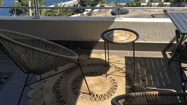 A balcony with wicker chairs, a woven rug, and a view of the sea. - Bastia : Apartment facing the sea, 2 beaches nearby  (San-Martino-di-Lota)
