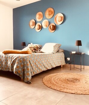 A bedroom with a bed, pillows, a bedside table, a lamp, and a wall with hats.