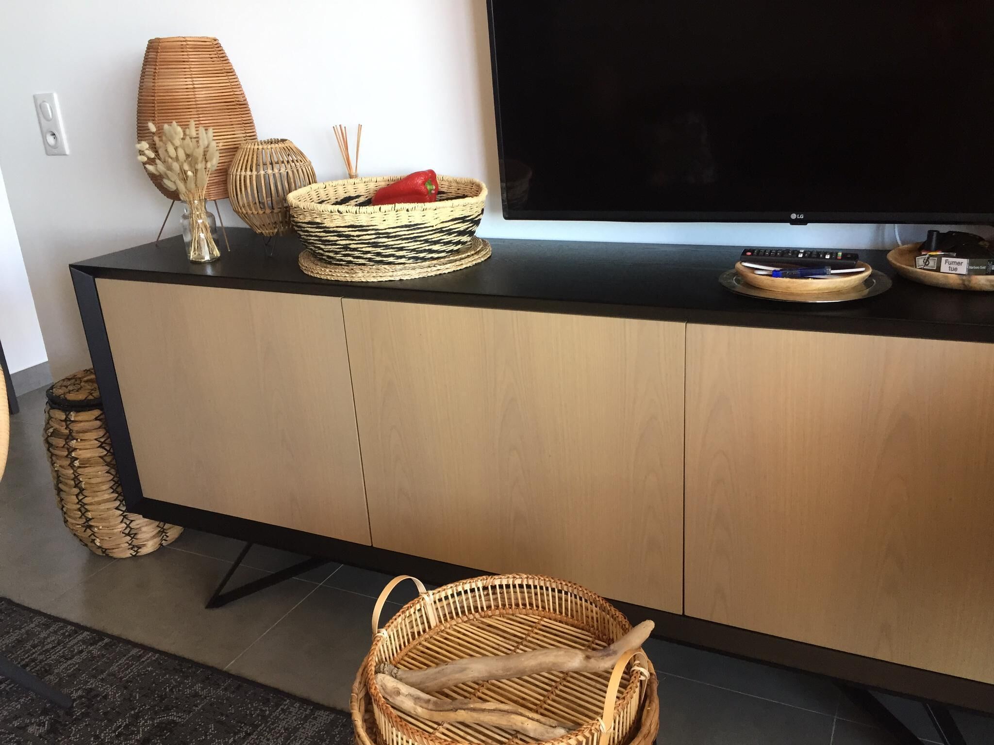 A modern living room with a black TV stand, wicker baskets, and a woven floor lamp.