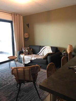 A living room with a sofa, a dining table, wicker chairs, a small side table, and a hanging light fixture.