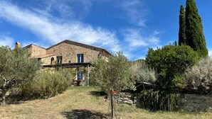 A stone building with a sloped roof, surrounded by dense vegetation and a clear blue sky. - Spectacular views from this villa for 8 in Valdorcia. Private Pool. (Sarteano)