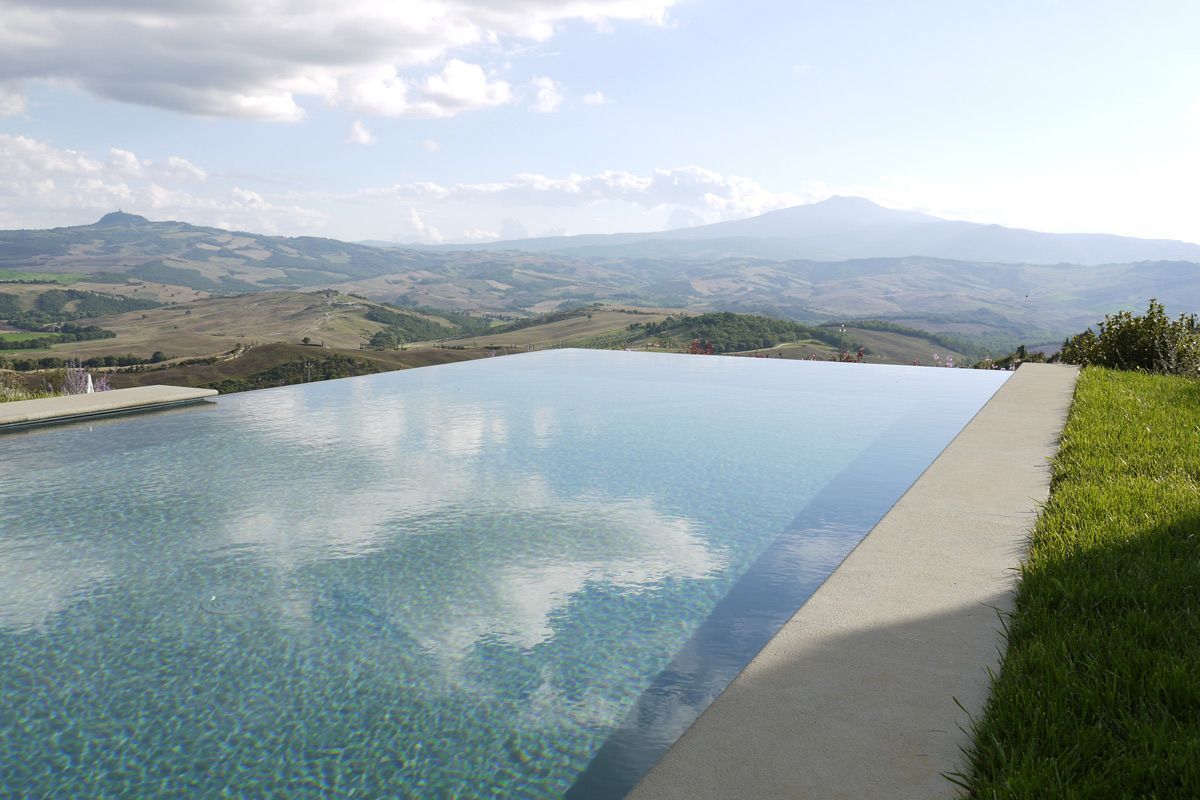 Ein klarer, rechteckiger Infinity-Pool mit Betonrand, umgeben von einer Rasenfläche und Blick auf sanfte Hügel und Berge in der Ferne.