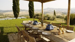 An outdoor dining area with a table set for four, surrounded by chairs, overlooking a scenic landscape with hills and a body of water. - Spectacular views from this villa for 8 in Valdorcia. Private Pool. (Sarteano)
