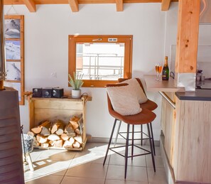 Una cocina acogedora con barra de madera, ventana con vistas, un taburete y chimenea con leña.