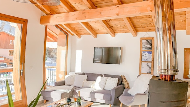 Ein gemütliches Wohnzimmer mit Holzbalkendecke, Kamin, einer Sofagarnitur und einem Fernseher.