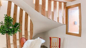 Ein Zimmer mit Holzboden, einer weißen Wand, einem Fenster, einem Sessel mit weißem Fellüberwurf und einem kleinen Topfpflanzen.