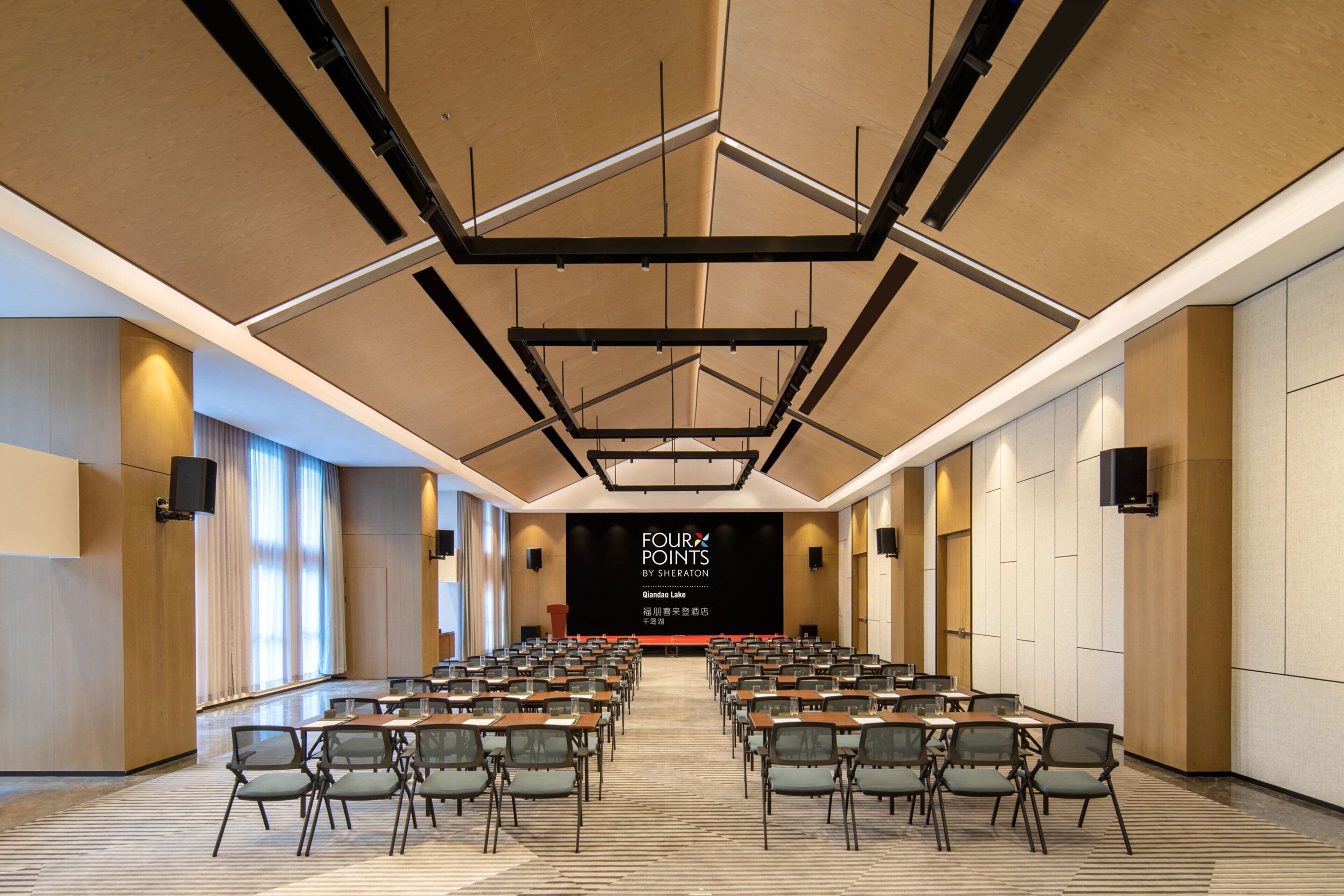 A conference room with a stage, rows of chairs, and a large screen displaying text.