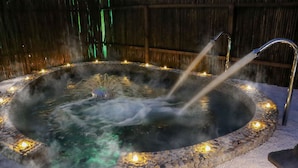 A hot spring bath surrounded by stones and candles, with a bamboo fence in the background.