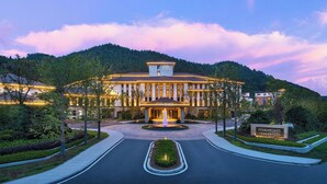 A hotel with a central fountain, surrounded by landscaped gardens and a mountainous backdrop.