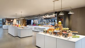 A modern hotel kitchen with multiple serving stations, a chef, and a variety of food items displayed.