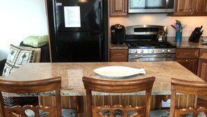 A kitchen with wooden cabinets, a black refrigerator, a stove, and a microwave. There are three wooden chairs with floral upholstery around a granite island. - Dog Friendly Townhome in the heart of Stone Harbor (Stone Harbor)