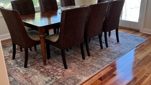A dining area with a wooden table and wicker chairs, a patterned rug, and large windows with blinds. - Dog Friendly Townhome in the heart of Stone Harbor (Stone Harbor)