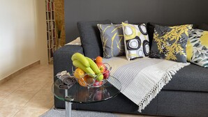 Ein modernes Wohnzimmer mit einer Couch, einem Glastisch mit Obst und einem Bücherregal.