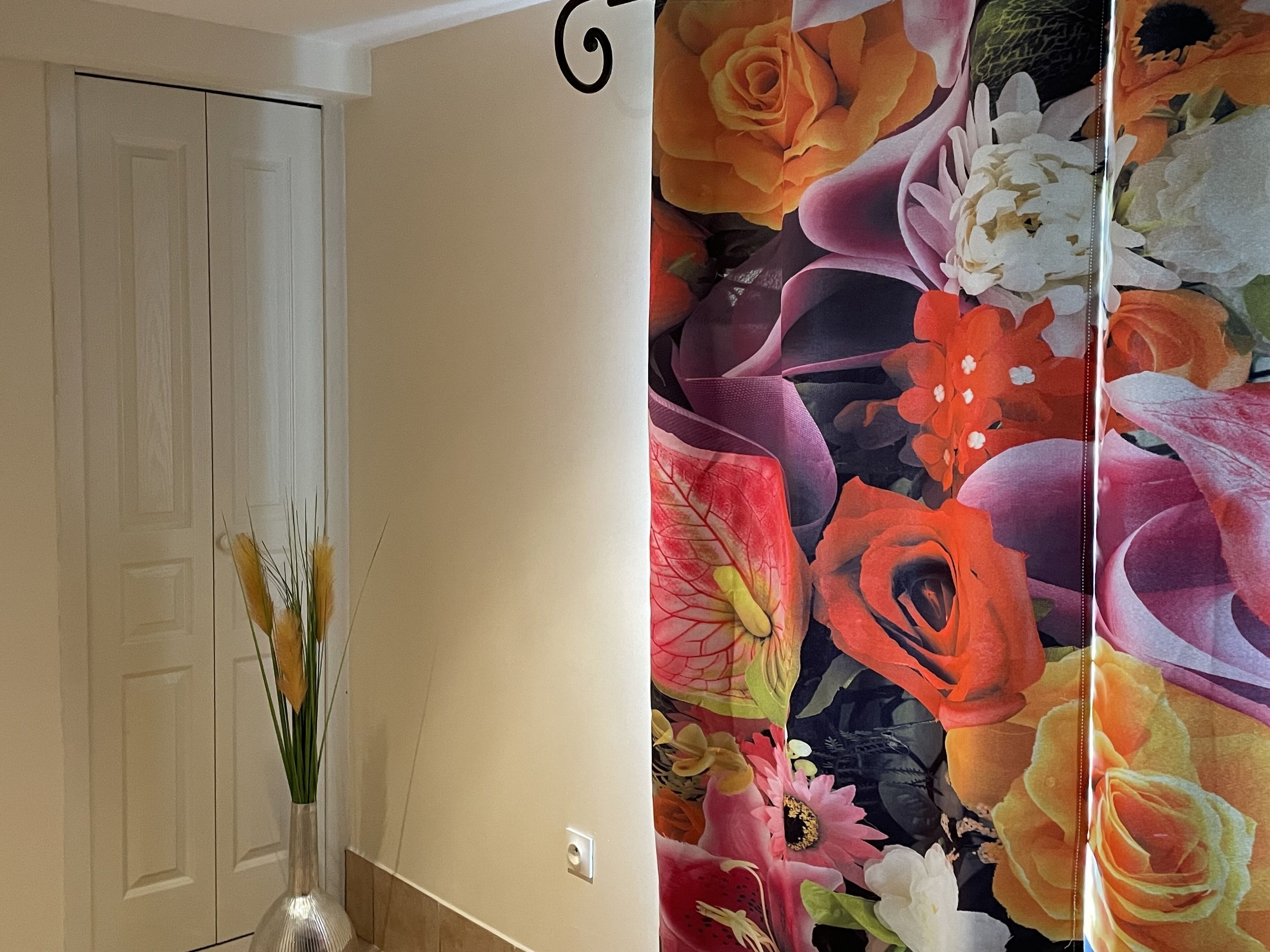 A hallway with a white door, a vase with flowers, and a floral-patterned wall.