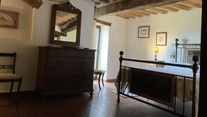 A room with a wooden dresser, a chair, a bed with a metal frame, and a ceiling with exposed beams.