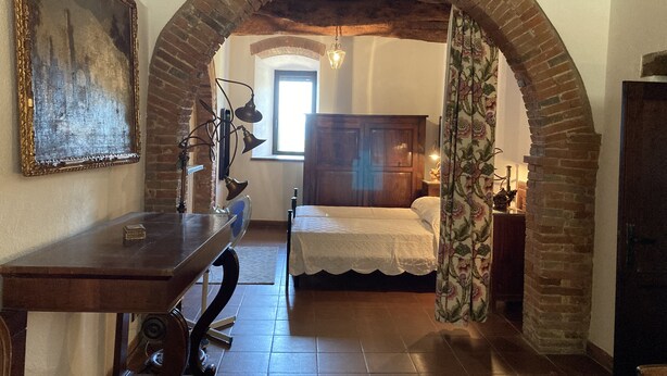 A room with a bed, a desk, a painting, and an arched brick structure.