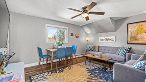 Un salon avec un ventilateur de plafond, un coin repas avec des chaises et une table, un canapé et un tapis.