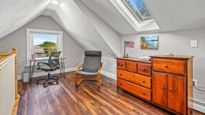 Une chambre à coucher aménagée dans un espace en hauteur, avec un puits de lumière, un bureau, une chaise, une commode et un tableau.