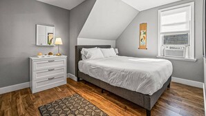 Une chambre à coucher avec un lit, une commode, un miroir et des œuvres d’art accrochées au mur.