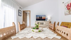 A living room with a wooden floor, a white doily, a television, a sofa, and a painting.