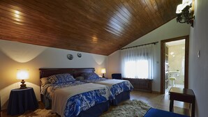 A bedroom with two beds, wooden ceiling, and a bathroom visible through an open door. - Finca Engracia Tranquilidad, Comodidad y Descanso (Cudillero)