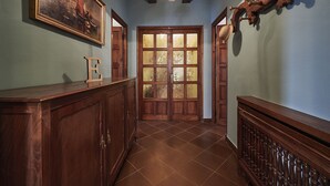 A hallway with a wooden reception desk, a framed painting, a chandelier, and a door with frosted glass panels. - Finca Engracia Tranquilidad, Comodidad y Descanso (Cudillero)
