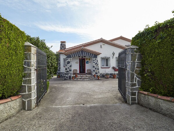 A stone house with a tiled roof, a red door, and a paved driveway leading to a gated entrance. - Finca Engracia Tranquilidad, Comodidad y Descanso (Cudillero)