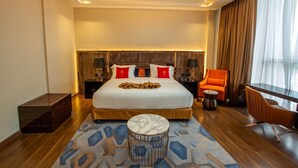 A modern hotel room with a large bed, two bedside tables with lamps, a round coffee table, a wooden bench, and a view of the city through large windows. - Hôtel Fleur de Lys Point E (Dakar)