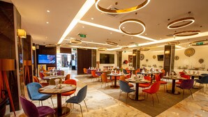 A modern restaurant with marble flooring, multiple dining areas with colorful chairs, and a TV screen in the background. - Hôtel Fleur de Lys Point E (Dakar)