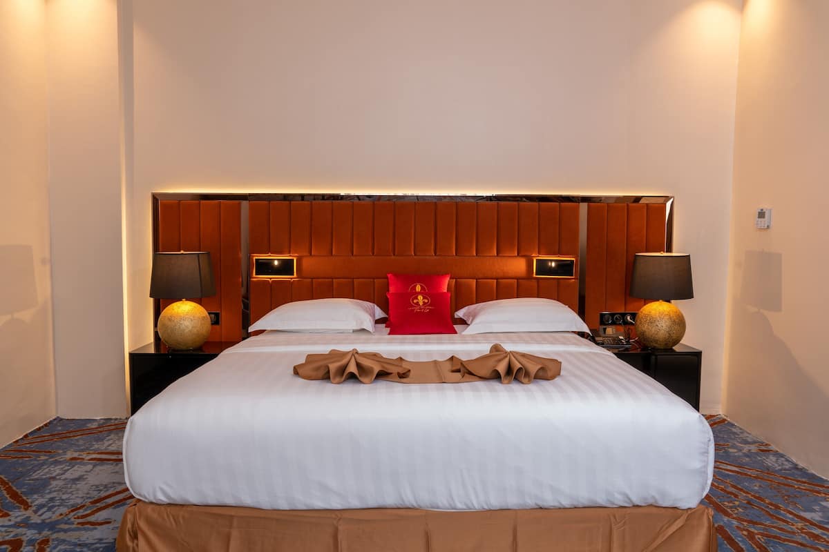 Una habitación de hotel con una cama grande, dos mesitas de noche, un cojín rojo decorativo y dos lámparas.