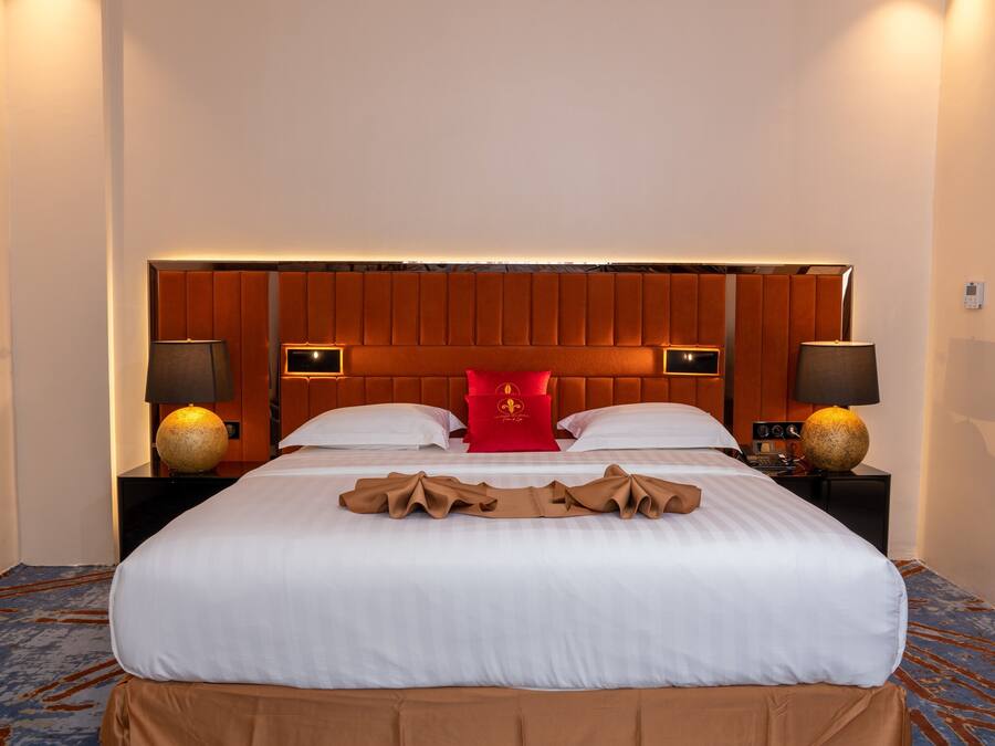 A hotel room with a large bed, two bedside tables, a red accent pillow, and two lamps.