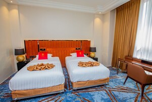 Habitación de hotel con dos camas, un cabecero de madera, un escritorio y una silla.
