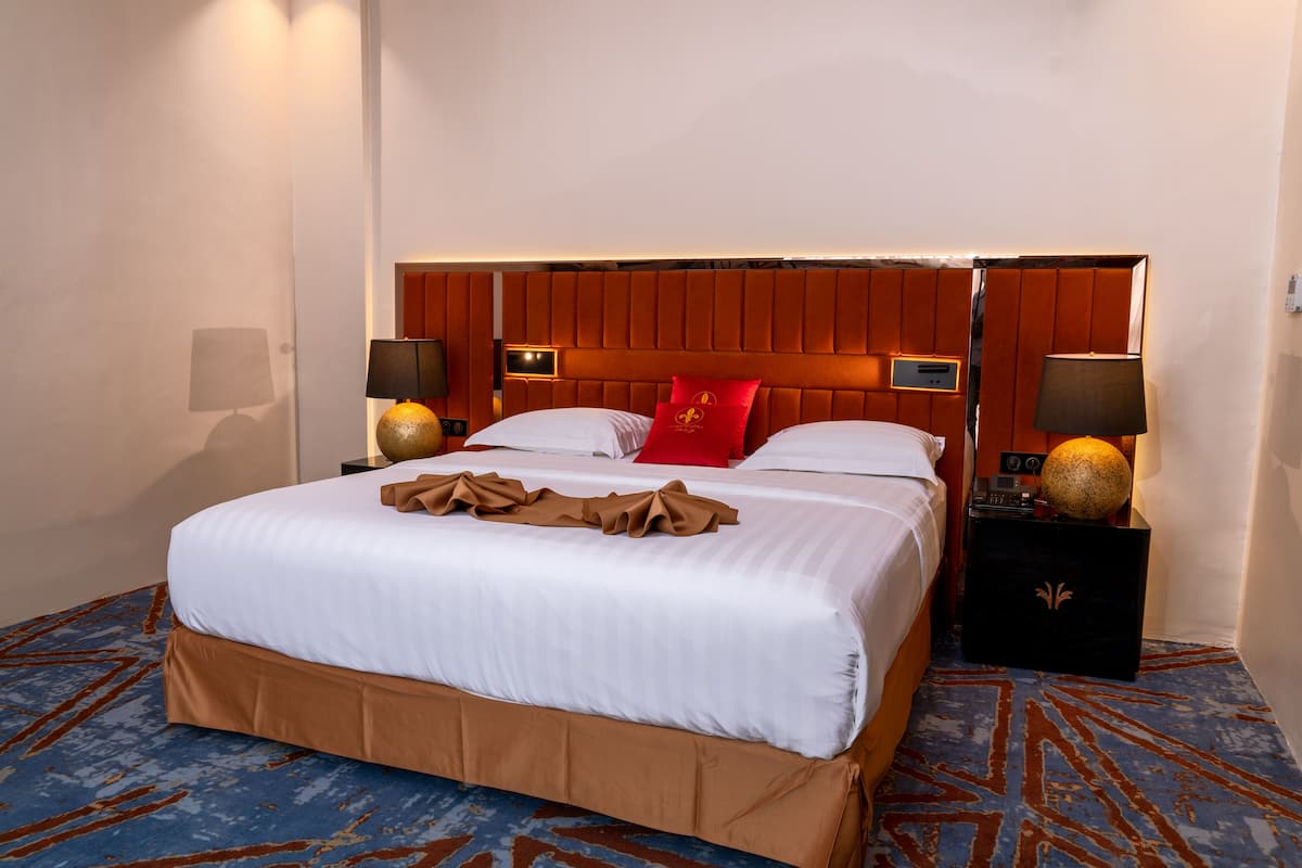 Habitación de hotel con una cama grande, dos mesitas de noche, un cabecero con iluminación integrada y una alfombra estampada.