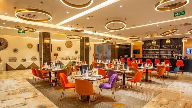 A modern restaurant with round tables, colorful chairs, and a bar area. - Hôtel Fleur de Lys Point E (Dakar)