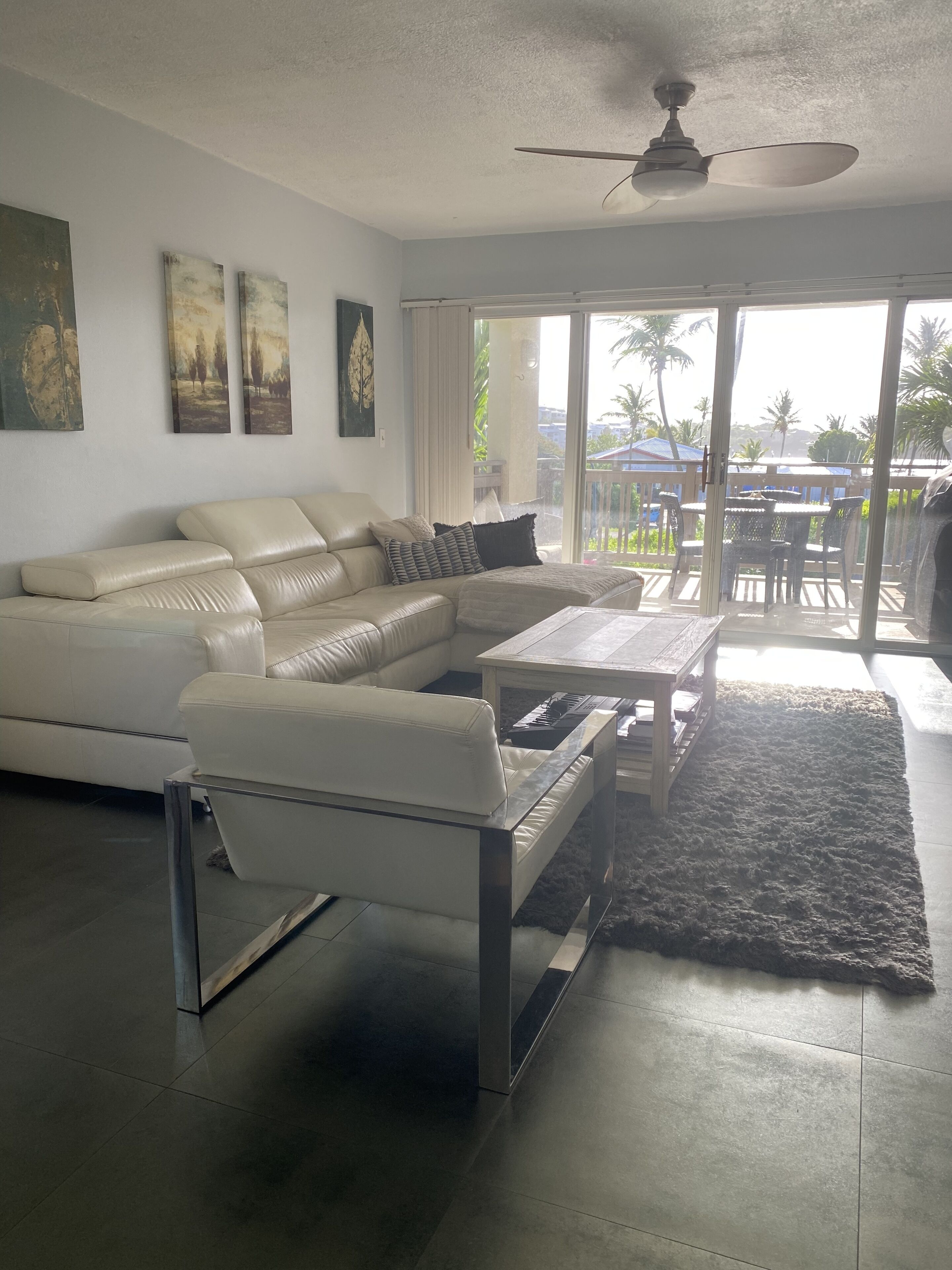 A modern living room with a white leather sofa, a glass coffee table, and a ceiling fan.