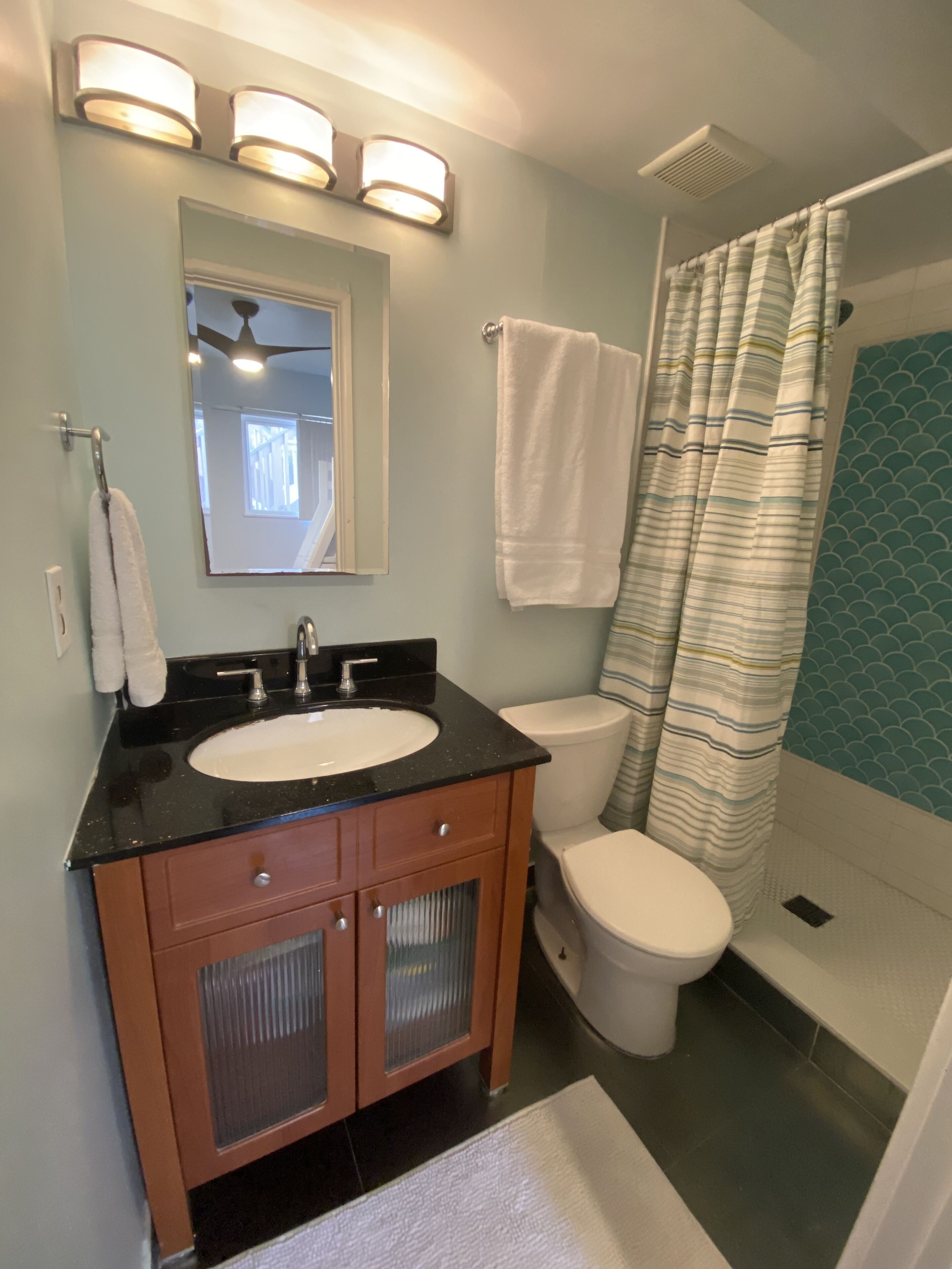 Un baño con un lavamanos negro, inodoro blanco y cortina de ducha.