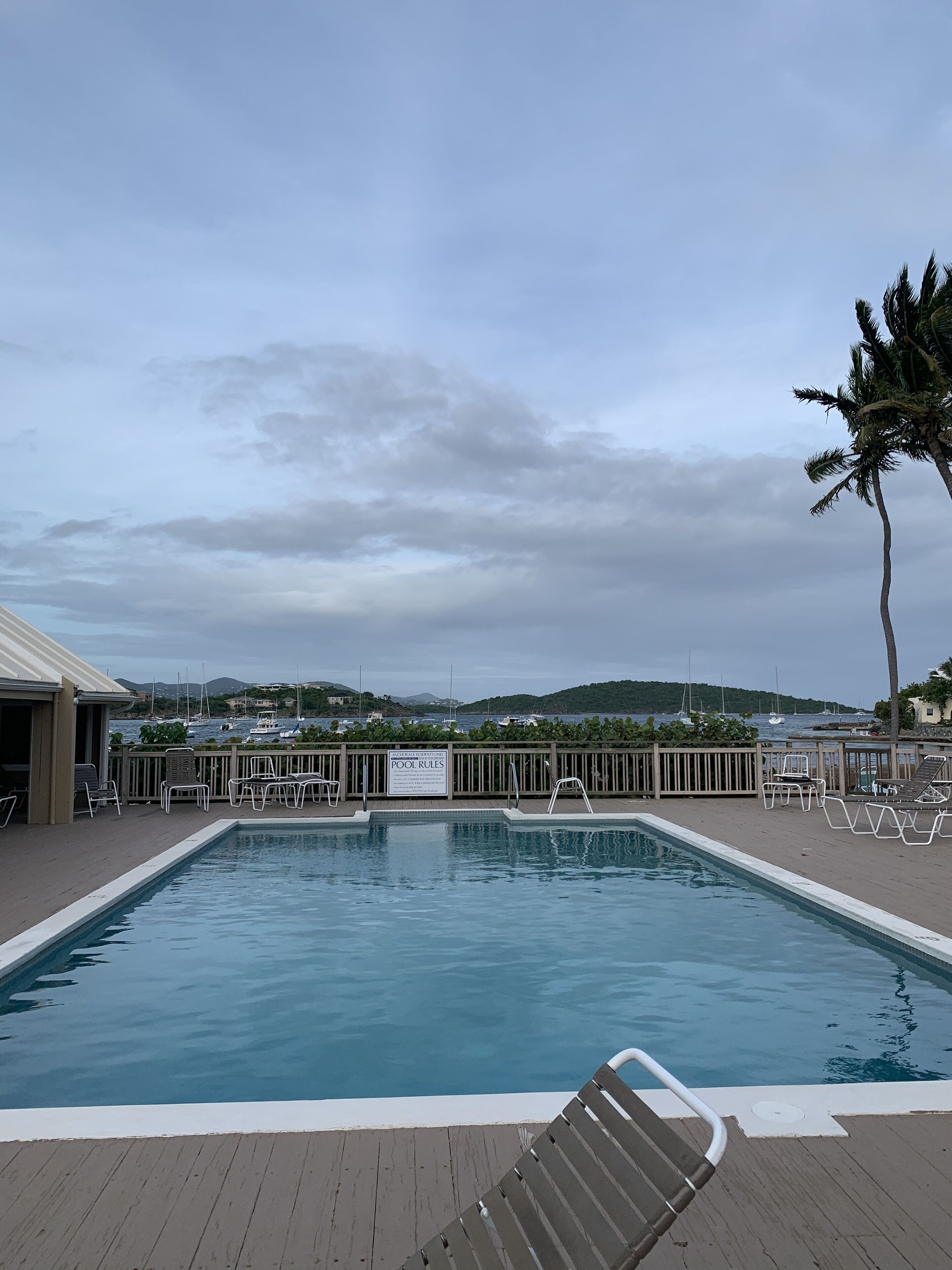 A swimming pool with a wooden deck, lounge chairs, and a sign indicating pool rules.